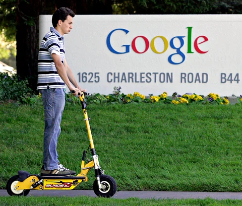 A man on an electric scooter passes by Google Inc.’s headquarters (Photographer: Kimberly White/Bloomberg News.)