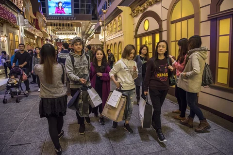 Shoppers carrying shopping bags walk past festive Christmas decorations near an entrance to Harbour City shopping mall, operated by Wharf Holdings Ltd., at night in the Tsim Sha Tsui district of Hong Kong, China (Photographer: David Paul Morris/Bloomberg) 