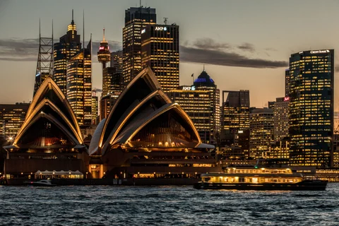The Sydney Opera House, foreground, and buildings in the financial district stand illuminated at dusk in Sydney, Australia. (Photographer: Cole Bennetts/Bloomberg)