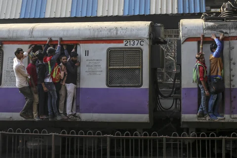 Passengers stand in the doorway, left, and on the side of train carriages as they travel by rail in Mumbai. (Photographer: Dhiraj Singh/Bloomberg)