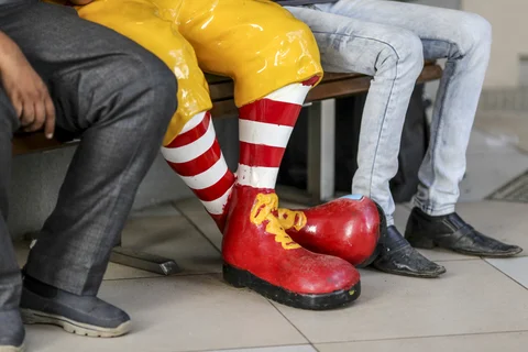 The legs and feet of food delivery couriers and a statue of Ronald McDonald are seen outside a McDonald’s Corp. restaurant. (Photographer: Dhiraj Singh/Bloomberg)