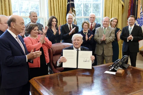 U.S. President Donald Trump holds up a signed memorandum on aluminium imports as Wilbur Ross, U.S. secretary of commerce, left, applauds in the Oval Office of the White House in Washington, D.C., U.S., on April 27, 2017. (Photographer: Olivier Douliery/Pool via Bloomberg)