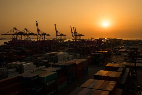 Containers sit stacked beneath gantry cranes. (Photographer: SeongJoon Cho/Bloomberg) 
