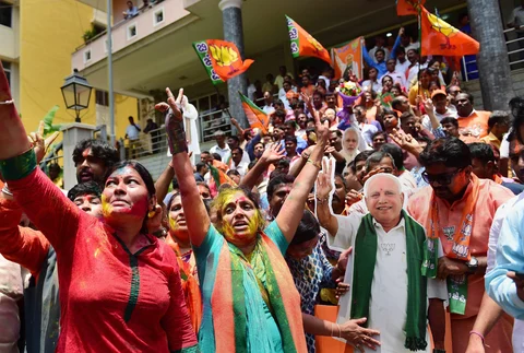 BJP workers, with a cut-out of chief ministerial candidate BS Yeddyurappa, celebrate the party’s lead on more than 110 Assembly seats, as the counting of votes is in progress, outside the party office in Bengaluru. (Source: PTI)