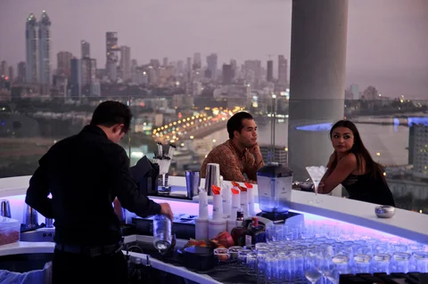 Customers sit next to a bar counter at the Aer rooftop bar at the Four Seasons Hotel against the city skyline in Mumbai. (Photographer: Kuni Takahashi/Bloomberg)