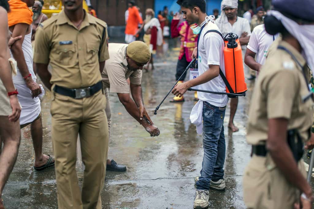 A street cleaner carrying a spray pack of disinfectant, assists a police officer cleaning his hands in Nashik, Maharashtra, India. (Photographer: Dhiraj Singh/Bloomberg)