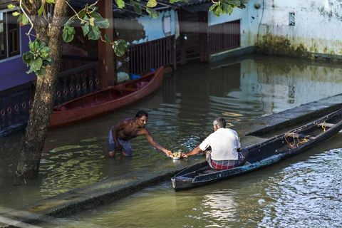 A man standing in floodwater shares a tray of tea with another man sitting in a canoe in Kainakary village in the district of Alappuzha, Kerala. (Photographer: Prashanth Vishwanathan/Bloomberg)
