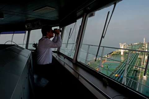 A crew member uses binoculars on the bridge of an oil tanker. (Photographer: Ali Mohammadi/Bloomberg)