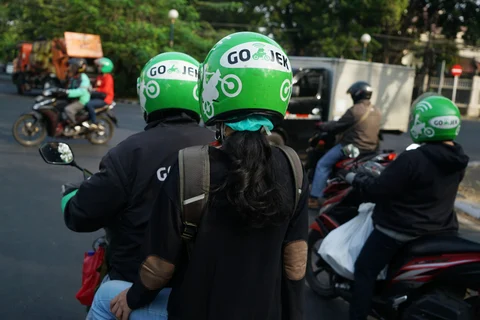 Go-Jek motorcycle taxi drivers and passengers travel through traffic in Jakarta, Indonesia. (Photographer: Dimas Ardian/Bloomberg)