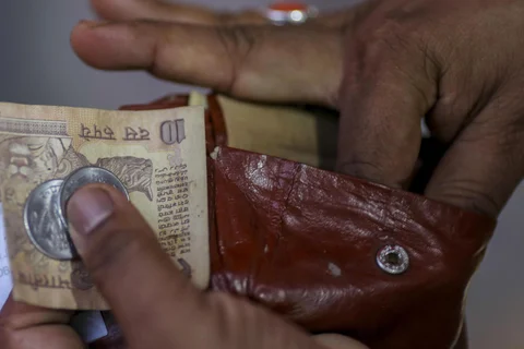 A man takes an Indian ten rupee banknote and one rupee coins out of a wallet in Mumbai. (Photographer: Dhiraj Singh/Bloomberg)