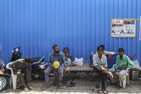 Construction workers sit at a perimeter fence in the Bhendi Bazaar area of Mumbai. (Photographer: Dhiraj Singh/Bloomberg)