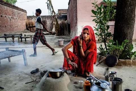 A resident of Pratapgarh district of Uttar Pradesh speaks on a mobile phone while she boils milk in an open kitchen. (Photographer: Sanjit Das/Bloomberg)
