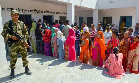 A security personnel stands guard as people wait in queues to cast their votes at a polling station during elections in Jammu, on Aug. 8, 2018. (Photograph: PTI)