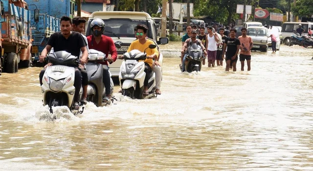 Two-wheeler riders and People wade through a flooded road following heavy monsoon rain at Panikhaiti in Kamrup district of Assam