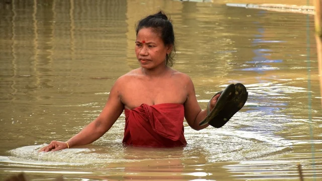A woman wades through a flooded area following heavy monsoon rain at Panikhaiti in Kamrup