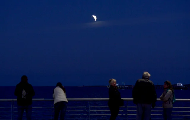 People watch the moon during a partial eclipse on the shore of the Rio de la Plata river in Buenos Aires on July 16, 2019.