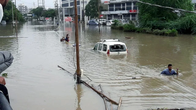 People cross a flooded road after the heavy rain at Ajitanagar in Vadodara, Gujarat