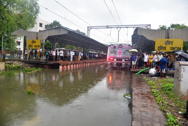 People wait for their train at flooded Sion Railway Station after heavy rainfall in Mumbai