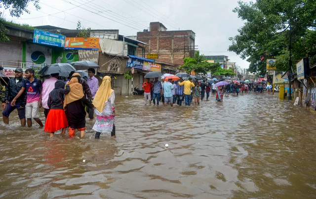 Pedestrians wade across a waterlogged street due to the overflow of Koyna river following monsoon rainfall, in Karad, Maharashtra