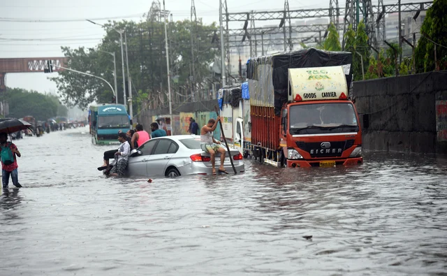 People sitting on a car on a flooded road after heavy rainfall at Sion in Mumbai