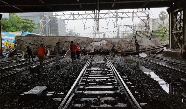 Railway and rescue workers gather around a site where a portion of a pedestrian footbridge collapsed over a railway track. / AFP PHOTO / Punit PARANJPE