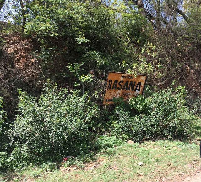 A battered iron board announces the entry to Patta Rasana village