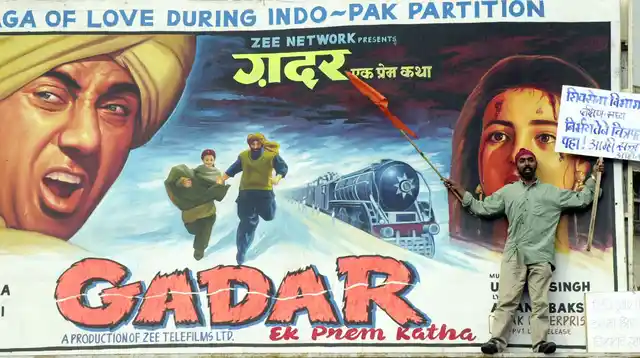 A Shiv Sena activist holds a banner exhorting people to see the movie ‘<i>Gadar-Ek Prem Katha</i>’ as he stands in front of a poster for the movie in Mumbai on June 27, 2001. (Photo: Reuters)