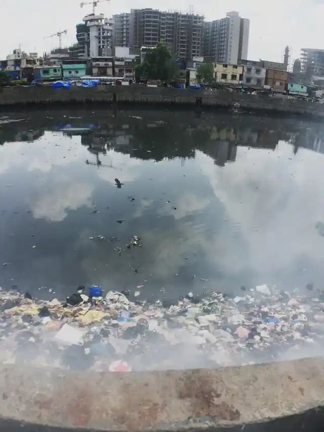 Burning trash piled up on the Mithi river, reaching the boundary wall. In the distance, Gyaneshwar Nagar, Bandra (East) slums, with the swanky Bandra-Kurla Complex, in the background. (Photo: <b>The Quint</b>/Pallavi Prasad)