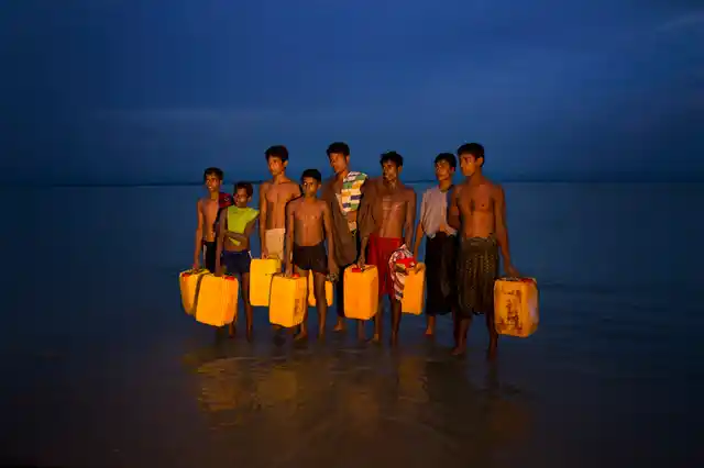 Newly arrived Rohingya Muslims carry yellow plastic drums they used as flotation aids and listen to Bangladeshi authorities