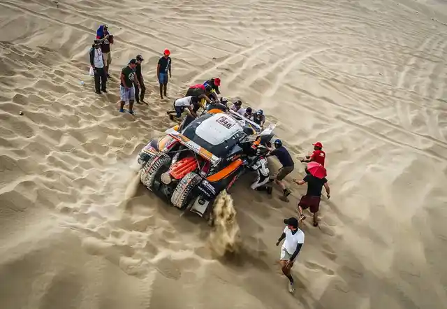 The Volvo team helps their driver as his car gets stuck in the sand.