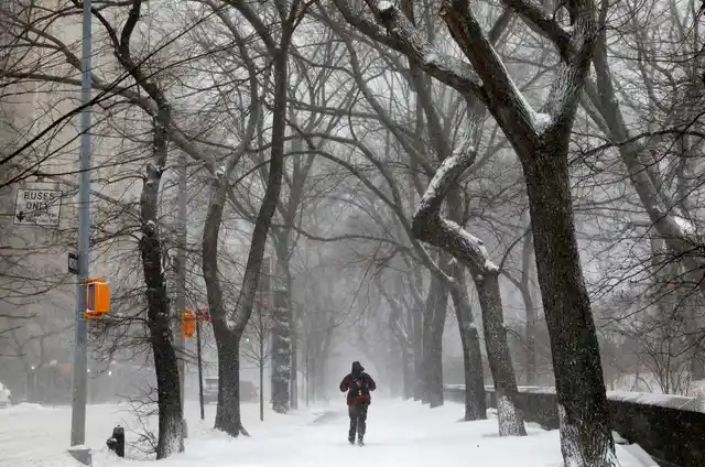 A man walks in the snow next to Central Park along 5th avenue in upper Manhattan during Storm Grayson in New York City, New York.