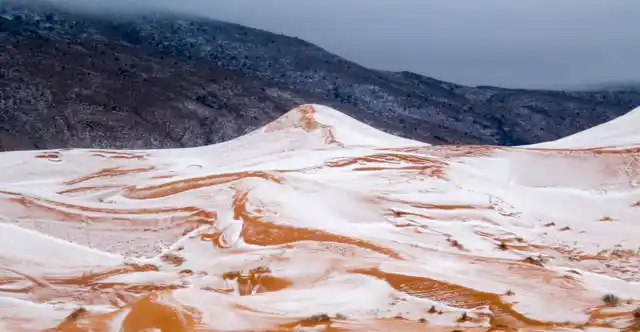 Smattering of snow on orange dunes.