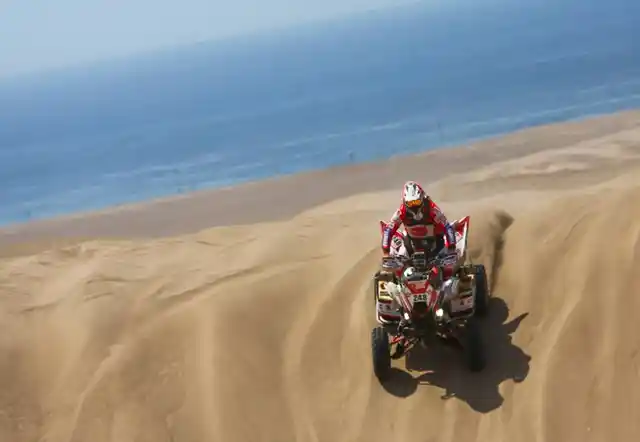 A quad biker coming down a sand dune. 