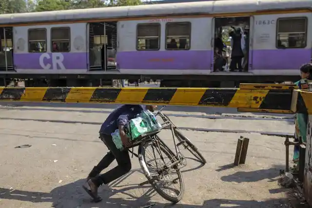 A cyclist ducks underneath the barrier of a railway crossing as a train travels past near Sewri railway station in Mumbai.
