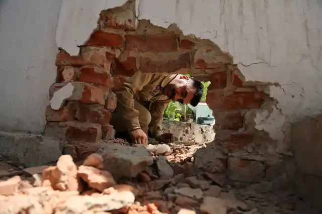 An Indian policeman looks at a hole made in a wall of a police station caused by a mortar shell.