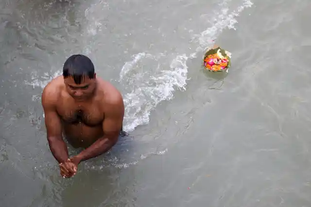 As a man takes a dip at Har Ki Pauri, devotional offerings disappear past him into the river.
