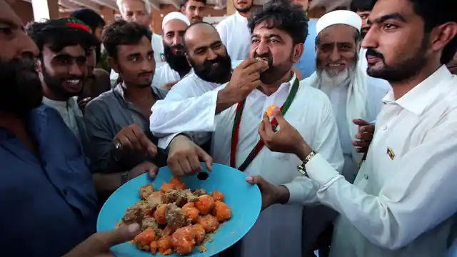Supporters of Pakistani politician Imran Khan, offer sweets to each other to celebrate the victory of their party candidate, in Peshawar, Pakistan.