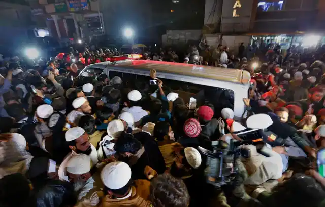 Haq’s followers crowding the van in which his body is being carried. 