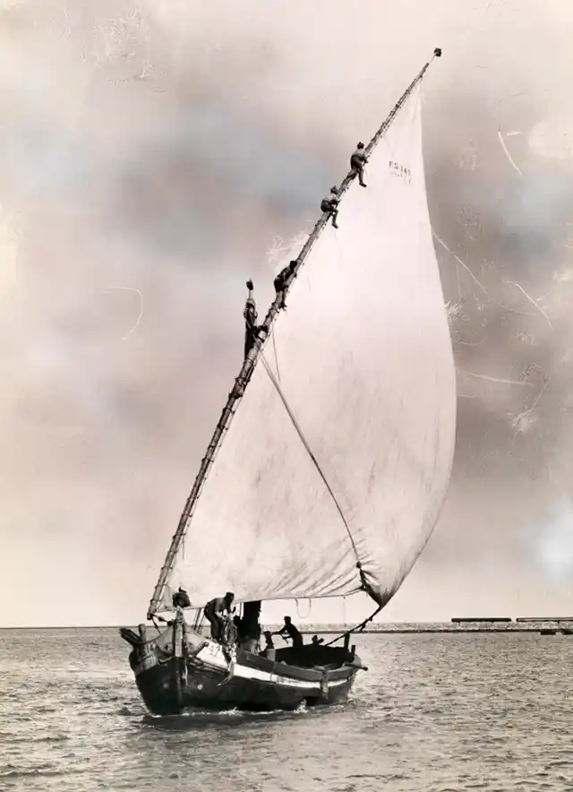 Men climb the mast of a fishing boat to furl the sail in Port Said, Egypt, 1924.