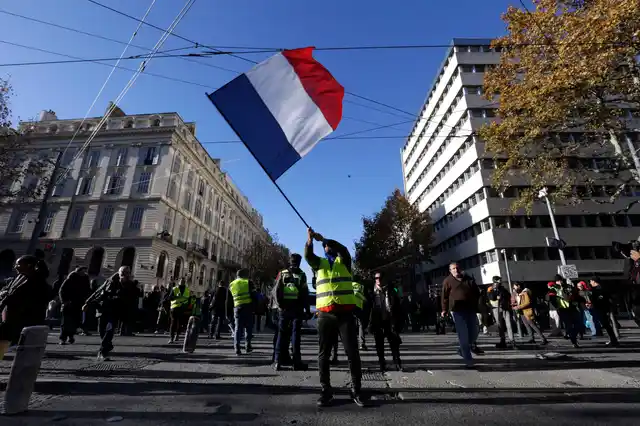 A demonstrator wearing a yellow vest waves the French flag during a march Saturday, 8 December, in Marseille, southern France. 