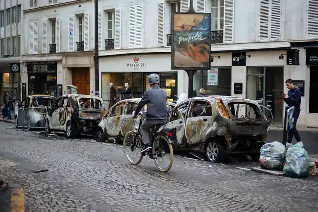 A man rides his bicycle past by charred cars near the Arc de Triomphe in Paris.