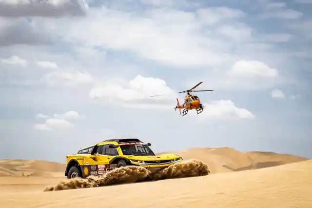 A car touches the ground, erupting sand from the impact.