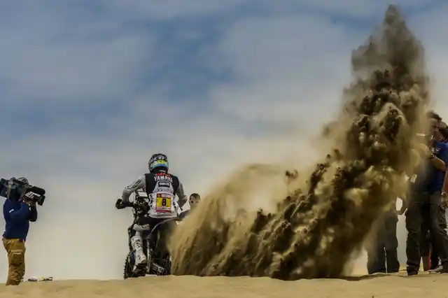 Sand erupts as a biker accelerates past his team.