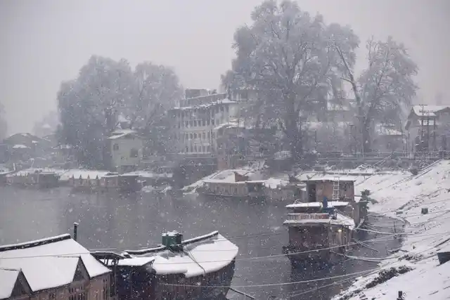 A man clears snow from roof top of houseboat at Jehlum river in Srinagar.