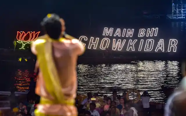 A priest is seen in the foreground as the BJP party symbol and election slogan illuminates Dashashwamedh Ghat on the eve of Prime Minister Narendra Modi’s election rally, in Varanasi.