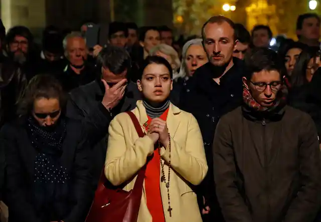 People pray as Notre Dame cathedral burns in Paris on Monday, 15 April, 2019.