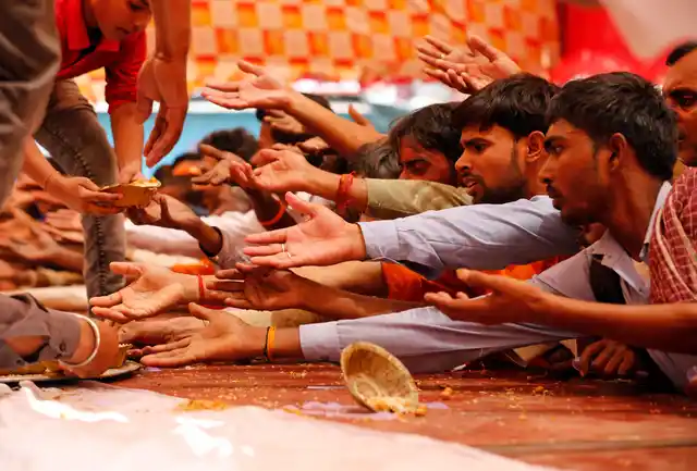 Passersby stretch out their arms to receive food distributed on a street to mark Bada Mangal in Lucknow.