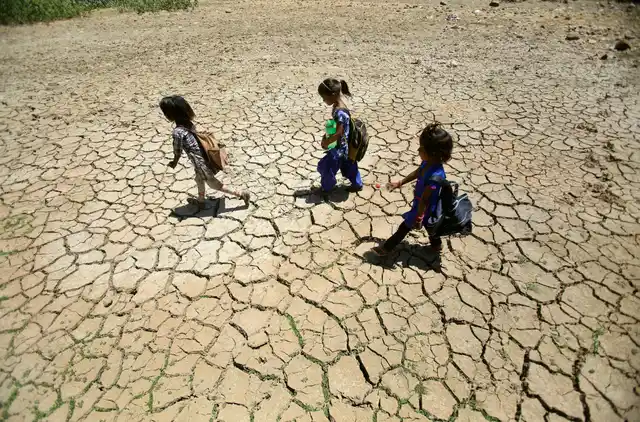 Children returning from school walk through a dried pond on a hot summer day on the outskirts of Jammu. 