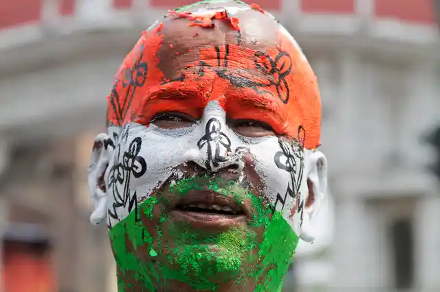 A Trinamool Congress party supporter stands with his face painted in the colors of the party flag, on a road leading to the residence of Chief Minister Mamata Banerjee in Kolkata. 