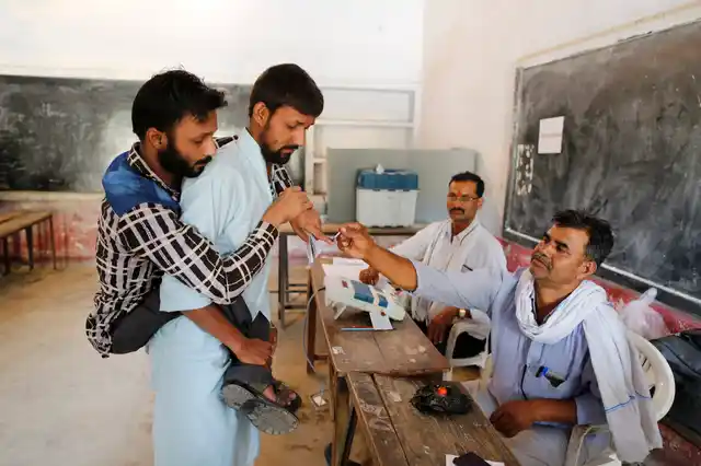 A polling officer puts indelible ink mark on the index finger of a differently able voter, carried by another man, in Prayagraj, Uttar Pradesh. 